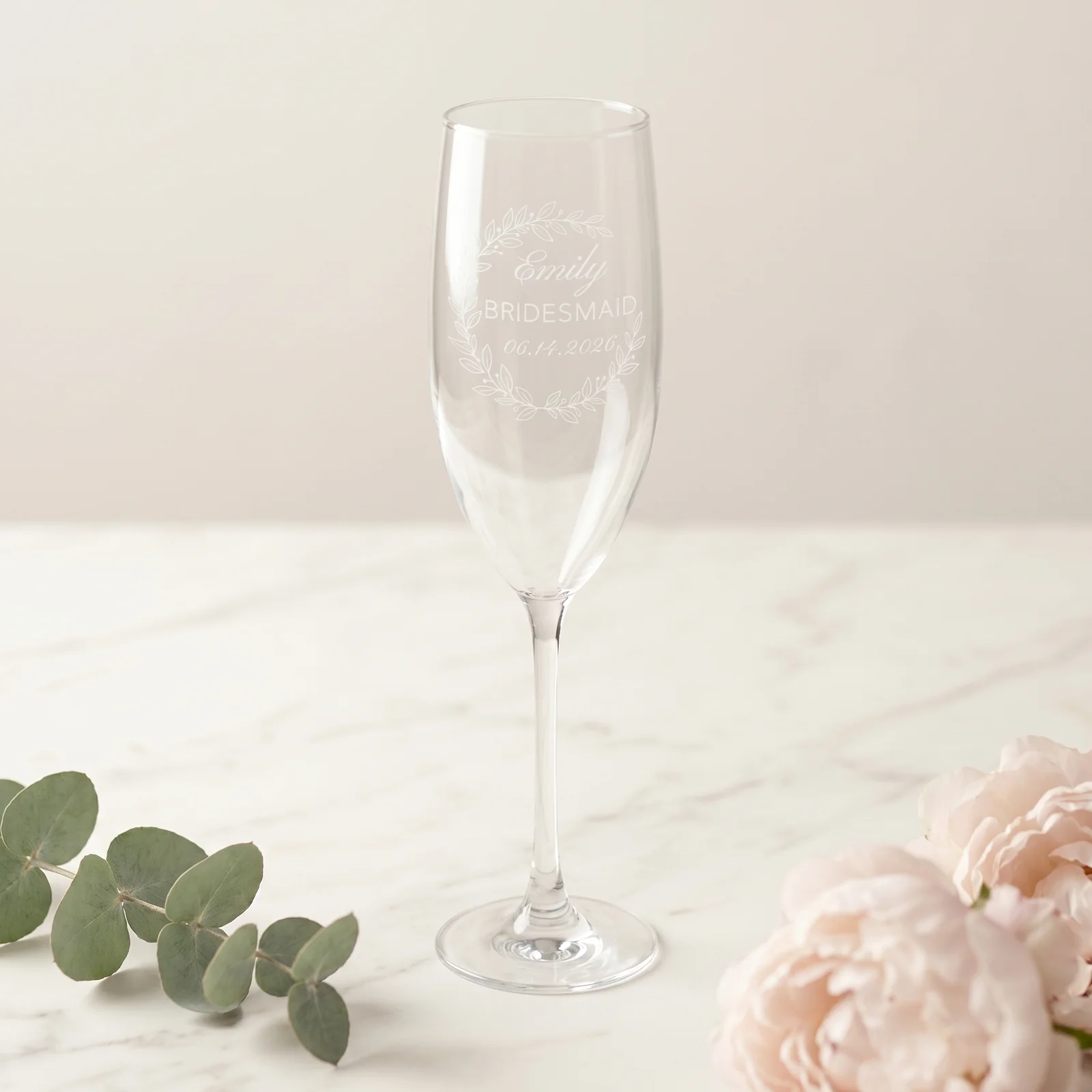 A personalized Eucalyptus Crescent Crest champagne flute resting in a kraft proposal box with a handwritten will-you-be-my-bridesmaid card and silk ribbon.